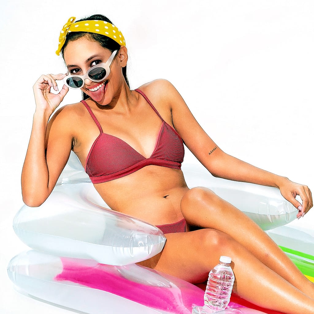 Young caucasian woman lying on a float mat sticking tongue out on a white set by commercial studio photographer Randy Schwartz