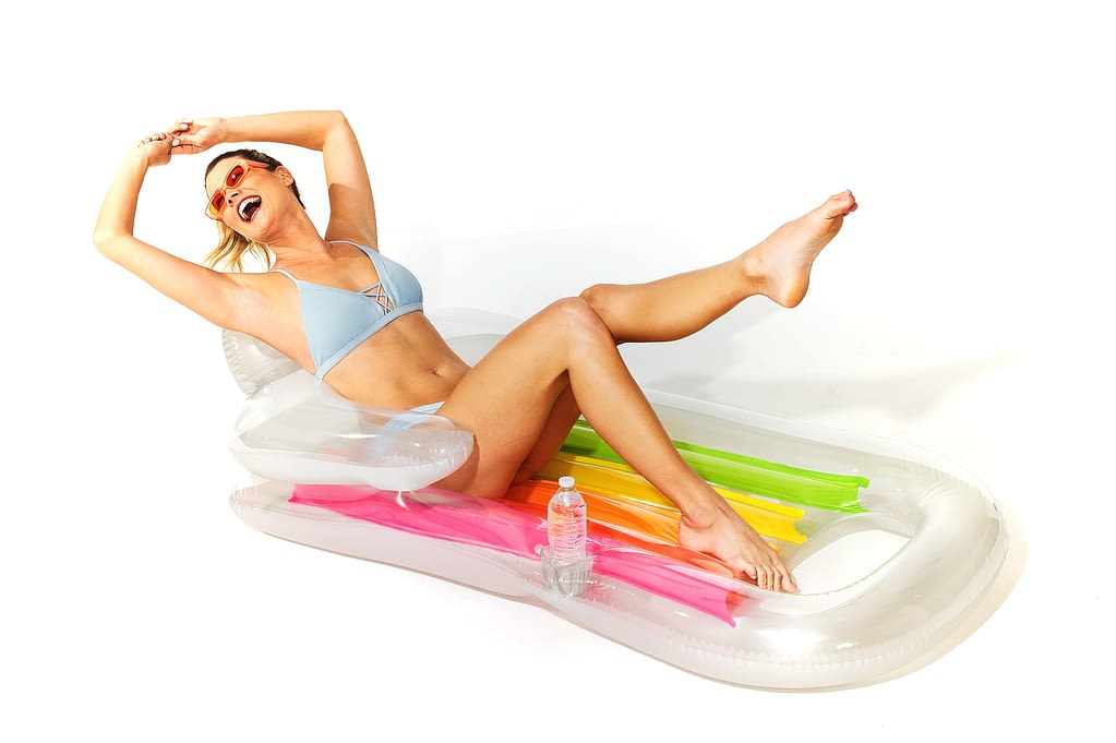 Young caucasian woman lying on a float mat laughing on a white set by commercial studio photographer Randy Schwartz